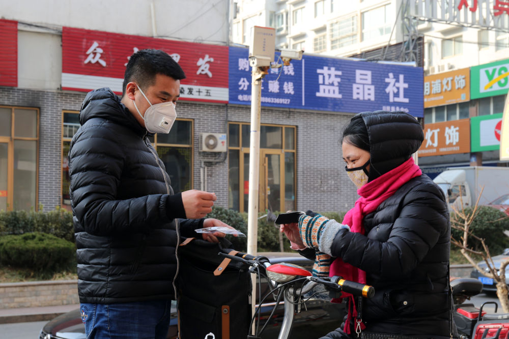 图为孙青云(右)在向市民分发口罩,并为其讲解口罩正确的使用方法
